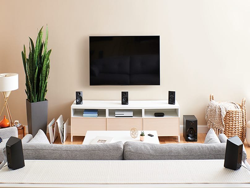Home cinema setup with speakers surrounding a TV in a bright living room